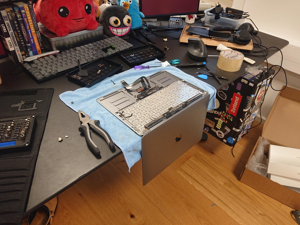 Macbook Air on a table, very messy, with many repair tools around