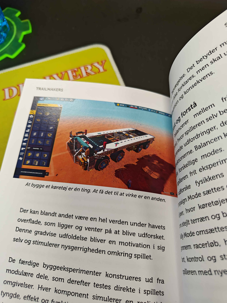 Book with picture of big vehicle from the game Trailmakers, with caption (translated) "Building vehicles is one thing. Making it work is another"