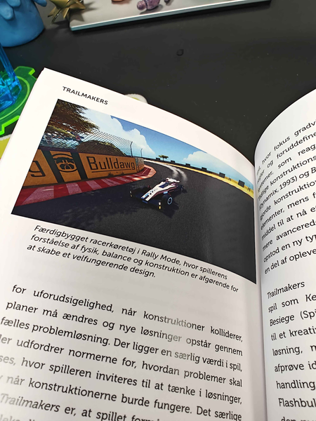 Book with picture of racing car from the game Trailmakers, with caption (translated) "Finished built racingcar in Rally Mode, wherein the players understanding of physics, balance and construction is crucial for creating a well functioning design"